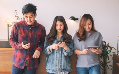 Cep telefonu ve tablet bilgisayarı kullanan ve ona bakan üç Asyalı genç.