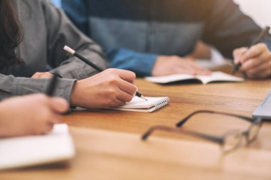 Boş deftere birlikte tahta masaya yazı yazan insanların yakın plan görüntüsü.