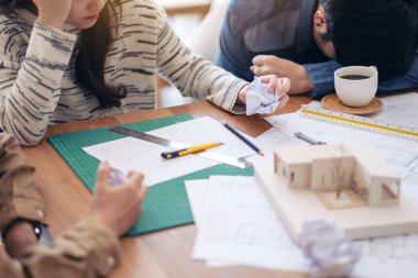 Bir grup mimar, mimarlık modeli üzerinde çalıştıktan sonra ofis masasında kağıt çizerken stresli hissediyorlar.