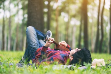 Yeşil bir bahçede uzanmış ukulele çalan bir adam