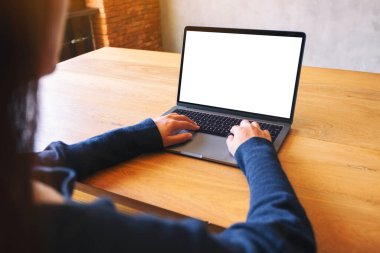 Laptop bilgisayar klavyesinde yazı yazan ve kullanan bir kadının resmi. Tahta masadaki boş beyaz masaüstü ekran. 