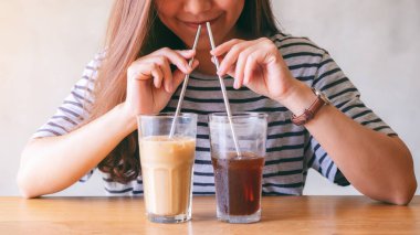 Aynı anda iki bardak buzlu kahve ve paslanmaz çelik pipetle içen Asyalı güzel bir kadının yakın plan görüntüsü.