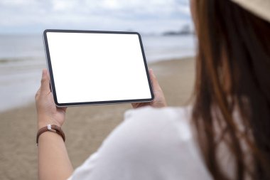 Deniz kenarında boş masaüstü ekranı olan siyah bir tableti tutan bir kadının görüntüsü