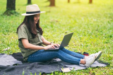Parkta otururken dizüstü bilgisayarında yazan Asyalı güzel bir kadın.