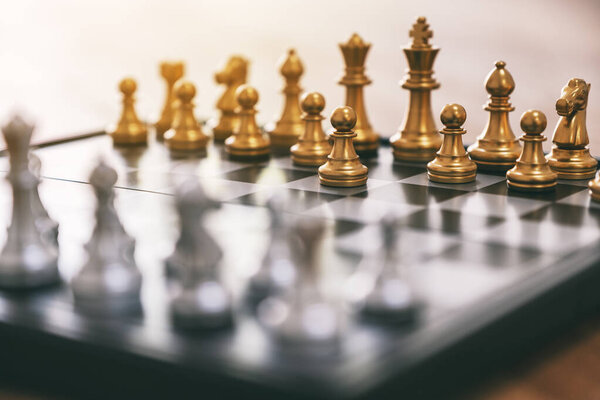 Closeup image of a silver and golden color chess set on chessboard