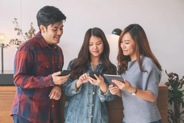 Cep telefonu ve tablet bilgisayarı kullanan ve ona bakan üç Asyalı genç.