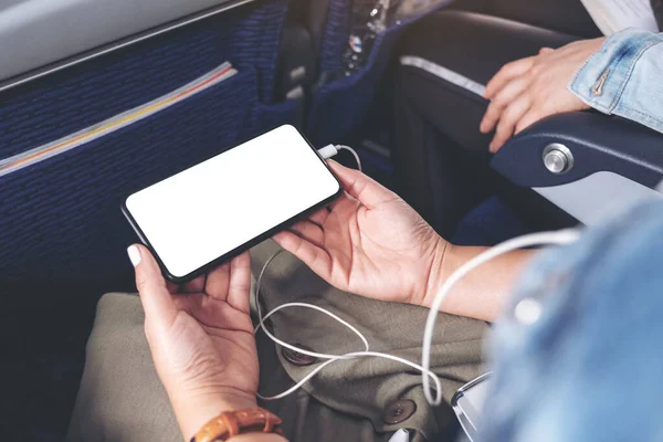 Mockup image of woman's hand holding a black smart phone with blank desktop screen and earphone in cabin