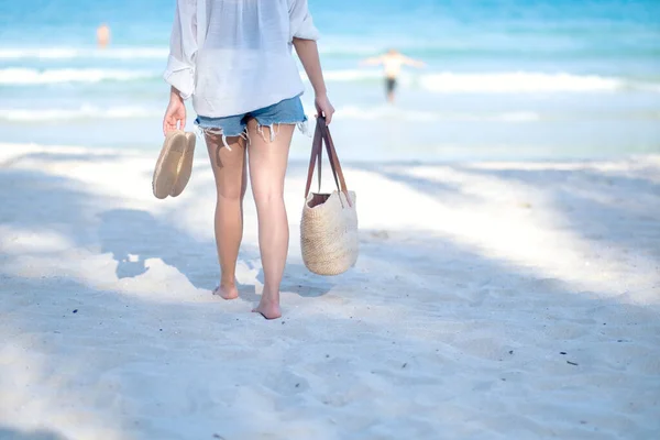 一个女人提着皮包和鞋子在沙滩上散步 带着大海和蓝天的背景 — 图库照片
