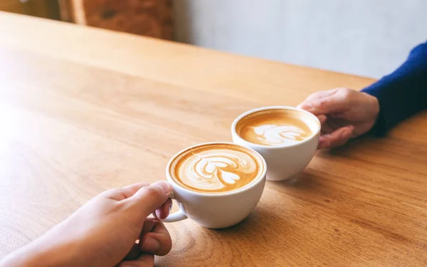 男と女のイメージを閉じます二つのコーヒーマグカップをクリックして木のテーブルの上にカフェ — ストック写真