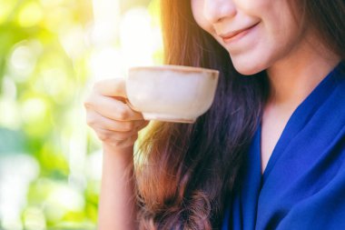 Bahçede sıcak kahve kokan ve içen Asyalı bir kadının yakın plan görüntüsü.