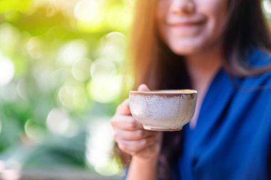 Bahçede elinde sıcak kahve tutan ve içen Asyalı bir kadının yakın çekimi.