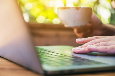 Kahve içerken bilgisayarda dokunan ve kullanan bir kadının yakın plan görüntüsü.