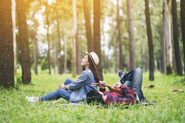 Genç bir çift ormanda birlikte oturup yatarken ukulele oynuyor.