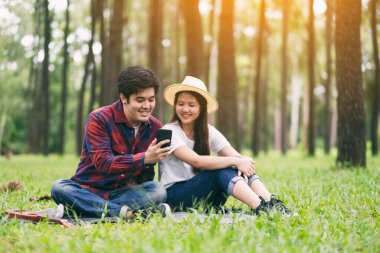 Parkta birlikte otururken cep telefonunu kullanan ve ona bakan genç bir çift.