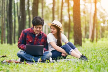 Genç bir çift parkta birlikte otururken dizüstü bilgisayara bakıp kullanıyor.