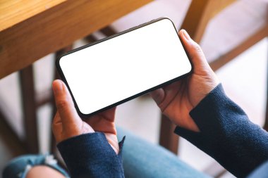 Kafede elinde siyah cep telefonu olan beyaz ekranlı bir kadının görüntüsü.