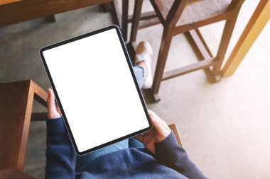 Kafede otururken elinde boş beyaz ekran olan siyah tabletli bir kadının üst görünüm görüntüsü