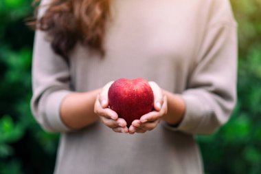 Elinde taze kırmızı bir elma tutan bir kadın.