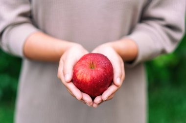 Elinde taze kırmızı bir elma tutan bir kadın.