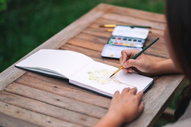 Bir kadın suluboya ile bir ağaç resmi çiziyor ve boyuyor