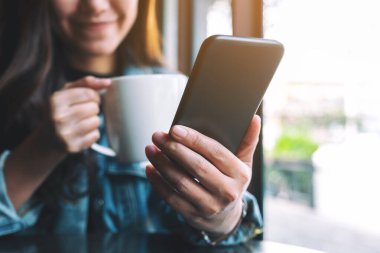 Kahve içerken cep telefonu kullanan bir kadının yakın plan görüntüsü.