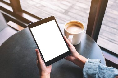Siyah tabletli, beyaz ekranlı ve masada kahve fincanı olan bir kadının görüntüsü. 