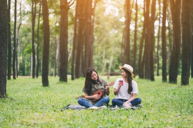 Ormanda birlikte otururken ukulele oynayan iki kadın.