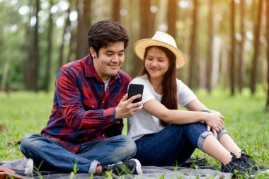 Parkta birlikte otururken cep telefonunu kullanan ve ona bakan genç bir çift.