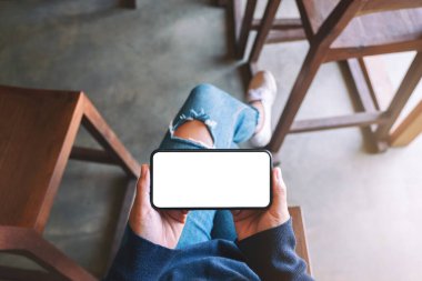 Kafede otururken elinde beyaz ekranlı siyah cep telefonu olan bir kadının üst görünüm görüntüsü