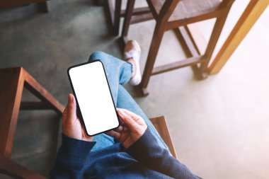 Kafede otururken elinde beyaz ekranlı siyah cep telefonu olan bir kadının üst görünüm görüntüsü