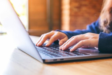 Ahşap masadaki dizüstü bilgisayarda çalışan ve daktilo kullanan bir kadının yakın plan görüntüsü.