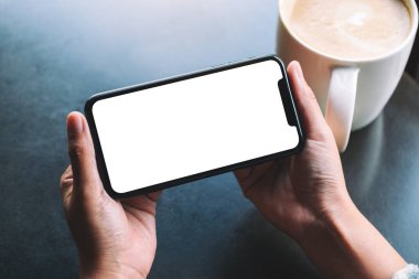 Masasında kahve fincanı olan, elinde siyah bir cep telefonu olan bir kadının görüntüsü.