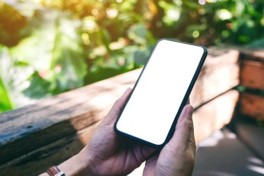 Açık havada boş masaüstü ekranı olan siyah cep telefonunu tutan ellerin görüntüsü