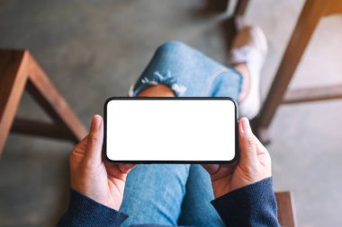 Kafede otururken elinde beyaz ekranlı siyah cep telefonu olan bir kadının üst görünüm görüntüsü