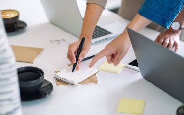 Bir grup işadamı ofisteki masadaki defteri tartışıyor, yazıyor ve işaret ediyor.