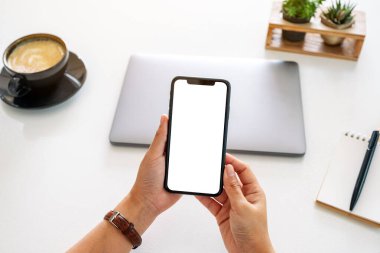 Ofisteki masada boş ekranlı ve dizüstü bilgisayarlı cep telefonu tutan ellerin en iyi görüntüsü.
