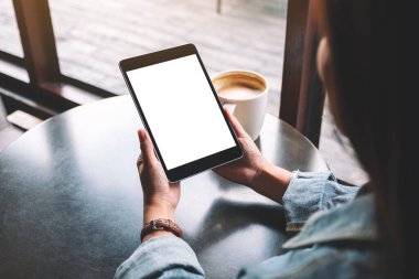 Siyah tabletli, beyaz ekranlı ve masada kahve fincanı olan bir kadının görüntüsü. 