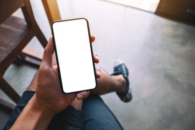 Kafede otururken elinde beyaz ekranlı siyah cep telefonu olan bir adamın görüntüsü.