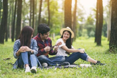 Parkta birlikte otururken ukulele oynayan bir grup genç.