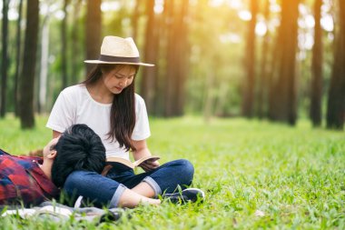 Genç Asyalı bir çift kitap okuyor ve parkta birlikte uzanıyorlar.