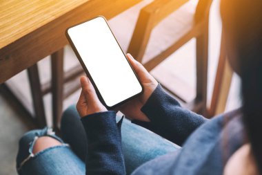 Kafede elinde siyah cep telefonu olan beyaz ekranlı bir kadının görüntüsü.