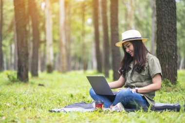 Parkta otururken dizüstü bilgisayarında yazan Asyalı güzel bir kadın.