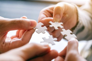 Beyaz yapbozun parçalarını bir araya getirip bir araya getiren birçok insanın yakın plan görüntüsü.