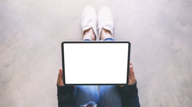 Üst görünümde, yerde otururken siyah tabletli beyaz ekranlı bir kadının görüntüsü var.