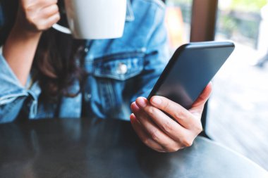 Kahve içerken cep telefonu kullanan bir kadının yakın plan görüntüsü.