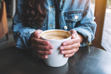 Masada elinde bir fincan sıcak kahve tutan bir kadının yakın plan görüntüsü.