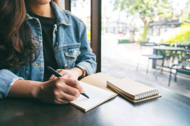 Masaya boş bir deftere yazı yazan bir kadının yakın plan resmi. 