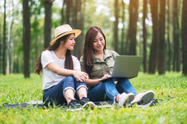 Parkta otururken dizüstü bilgisayar kullanan iki Asyalı kadın.