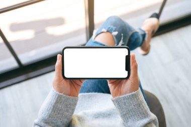 Beyaz masaüstü ekranlı siyah bir cep telefonu tutan bir kadının üst görünüm görüntüsü 