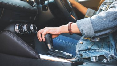 Yakından bakınca, araba sürerken otomatik vites kolu değiştiren bir kadın sürücü görülüyor.